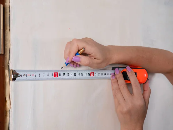 A woman measuring the wall with a measuring tape, close-up.