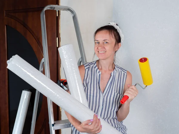 A happy woman holds rolls of new Wallpaper in her hands. Repairs in the apartment. Wallpapering.