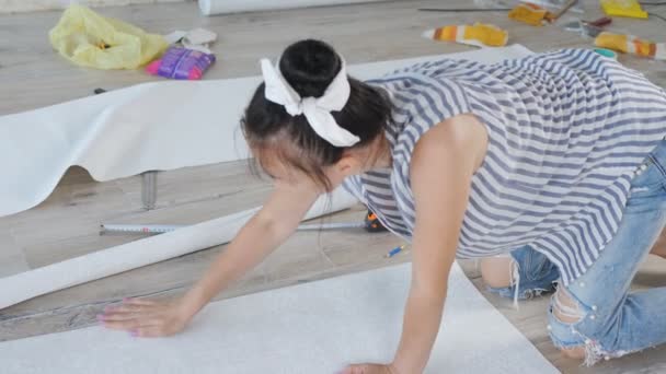 A woman sitting on the floor with scissors cuts a strip from a roll of Wallpaper for pasting Wallpaper on the wall during repairs in the room. — Stock Footage A woman sitting on the floor with scissors cuts a strip from a roll of Wallpaper for pasting Wallpaper on the wall during repairs in the room. Royalty Free Stock Video