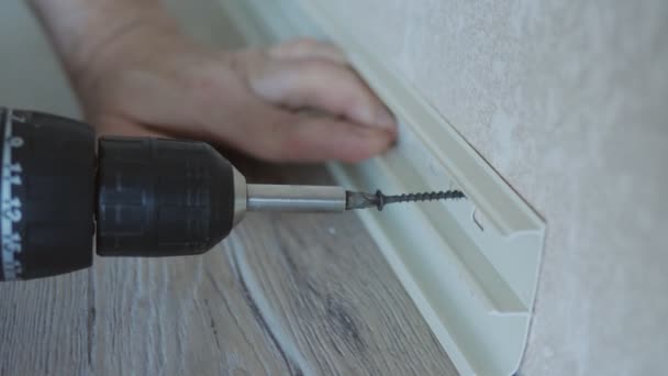 The master installs the skirting Board on the plasterboard wall in the room. Close-up of screwing a self-tapping screw into drywall. Installation of skirting boards in the apartment. — Stock Footage The master installs the skirting Board on the plasterboard wall in the room. Close-up of screwing a self-tapping screw into drywall. Installation of skirting boards in the apartment. Video Clip