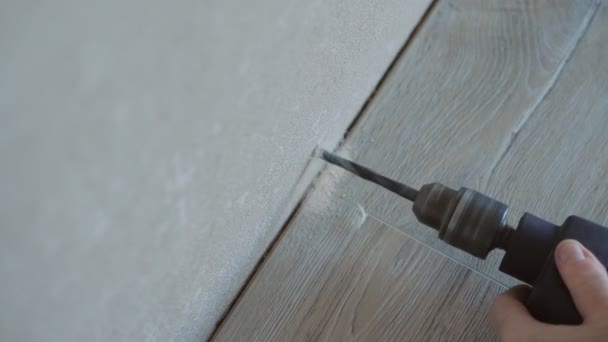 Technology installation of plastic floor length on drywall, master drill a hole in the wall using a drill, inserts a screw, twists, fastens baseboard to wall, repairs — Stock Footage Technology installation of plastic floor length on drywall, master drill a hole in the wall using a drill, inserts a screw, twists, fastens baseboard to wall, repairs Stock Footage