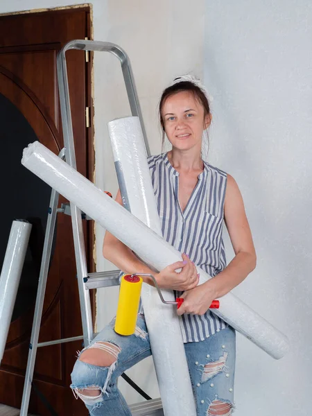 Repairs in the apartment. Wallpapering. Portrait of a woman with rolls of Wallpaper near the stepladder in the room.