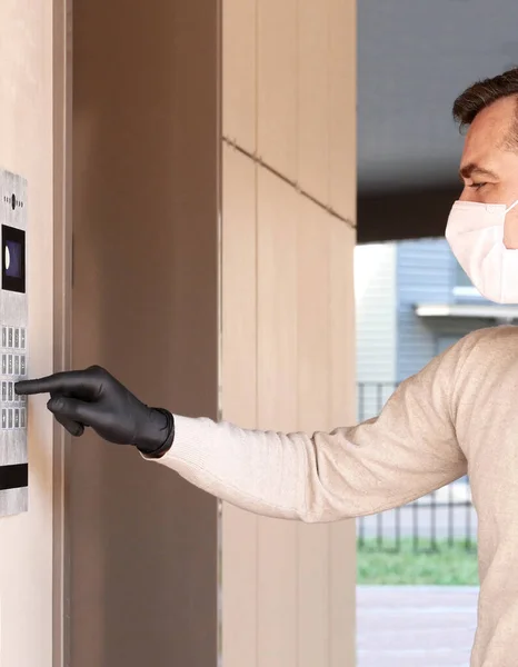 Man in face mask and gloves dials the code on the intercom and going in porch of his apartment. Pandemic covid-19 concept — Stock Photo, Image