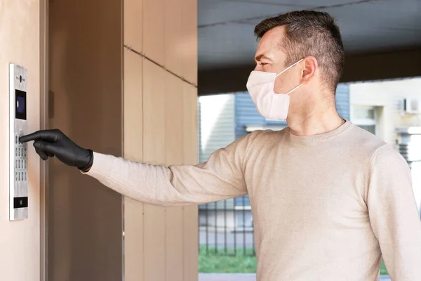 Man in face mask and gloves dials the code on the intercom and going in porch of his apartment. Pandemic covid-19 concept — Stock Photo, Image