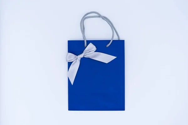 A blue gift bag with a silver ribbon on white background. Top view, copy space. Gift concept. New year, Woman\'s day. Valentine\'s day. Ready for birthday party.