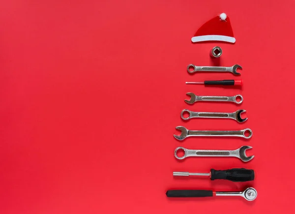 Christmas tree made of construction tools with a New Years red hat on a red background. New Year Concept for auto workshop. Flat lay, copy space, top view