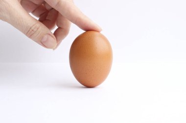 Parmak bir dikey durumda hafif bir arka plan üzerinde izole kahverengi tavuk yumurta tutar