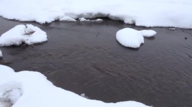 Karla kaplı sahilleri arasında donmamış dere akar. 