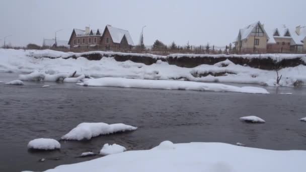 Χειμερινό τοπίο - παγωμένα ποταμός ρέει ανάμεσα σε απότομες όχθες παρελθόν εξοχικών κατοικιών. — Αρχείο Βίντεο