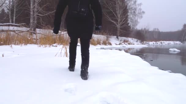 En tjej går i djup snö längs stranden av en frusen flod. — Stockvideo