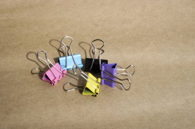 Kaba kahverengi kraft kağıt arka planda farklı renklerde kağıt klipleri. Kırtasiye. Metin için kopyalama alanı ile.