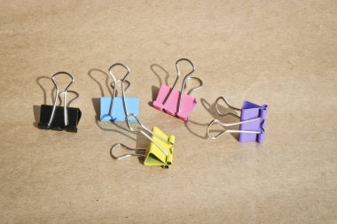 Kaba kahverengi kraft kağıt arka planda farklı renklerde kağıt klipleri. Kırtasiye. Metin için kopyalama alanı ile.