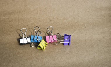 Kaba kahverengi kraft kağıt arka planda farklı renklerde kağıt klipleri. Kırtasiye. Metin için kopyalama alanı ile.