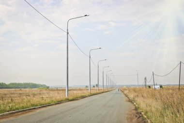 Asfalt yol ve yol kenarında fenerler ve sıcak güneş ışığında mesafe yalnız bir bisikletçi. Seyahat ve macera kavramı.