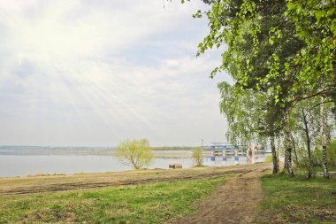 Loş güneş ışığı ve baraj görünümünde sabahın erken saatlerinde huş ağaçları ile rezervuar kıyısı. Doğanın uyumu ve insan aktivitesi kavramı.