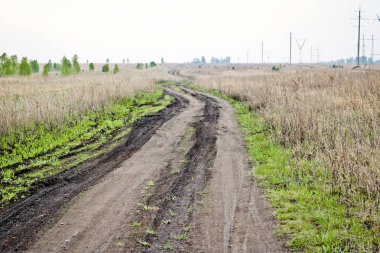 Erken ilkbaharda tarlalar arasında kirli kırık toprak yol. Seyahat ve macera kavramı.
