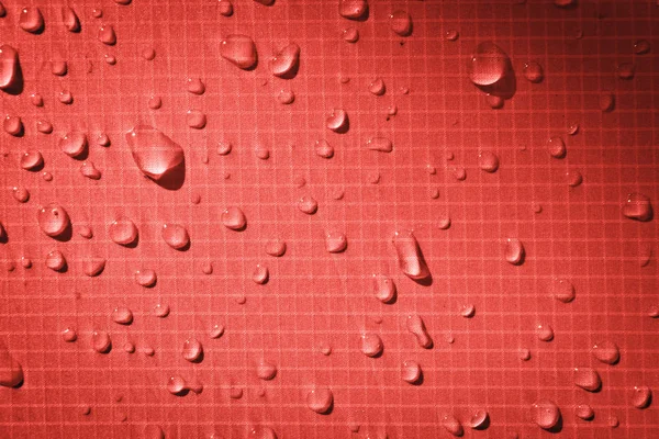 Large drops of water on a red textile with a waterproof effect. Water-repellent impregnation. Texture drops on the fabric.