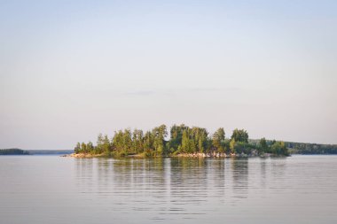 Gün batımı ışınları sakin bir dağ gölü üzerinde huş ormanı ile büyümüş Rocky ada.