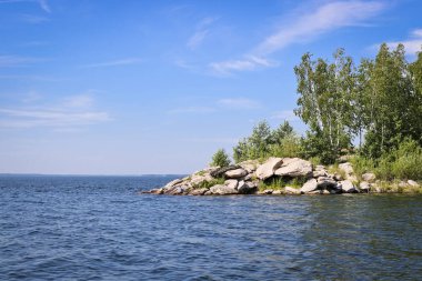 Gölün yüzeyi kayalık bir kıyıya karşı dalgalar ve dalgalar ile kaplıdır. Güneşli havalarda yaz manzarası.
