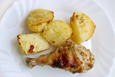 Fırında tavuk budu ve beyaz bir tabakta patates. Seçici odak.