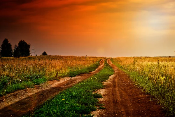A gloomy field road in the middle of the countryside in dramatic evening light. Summer somber landscape.