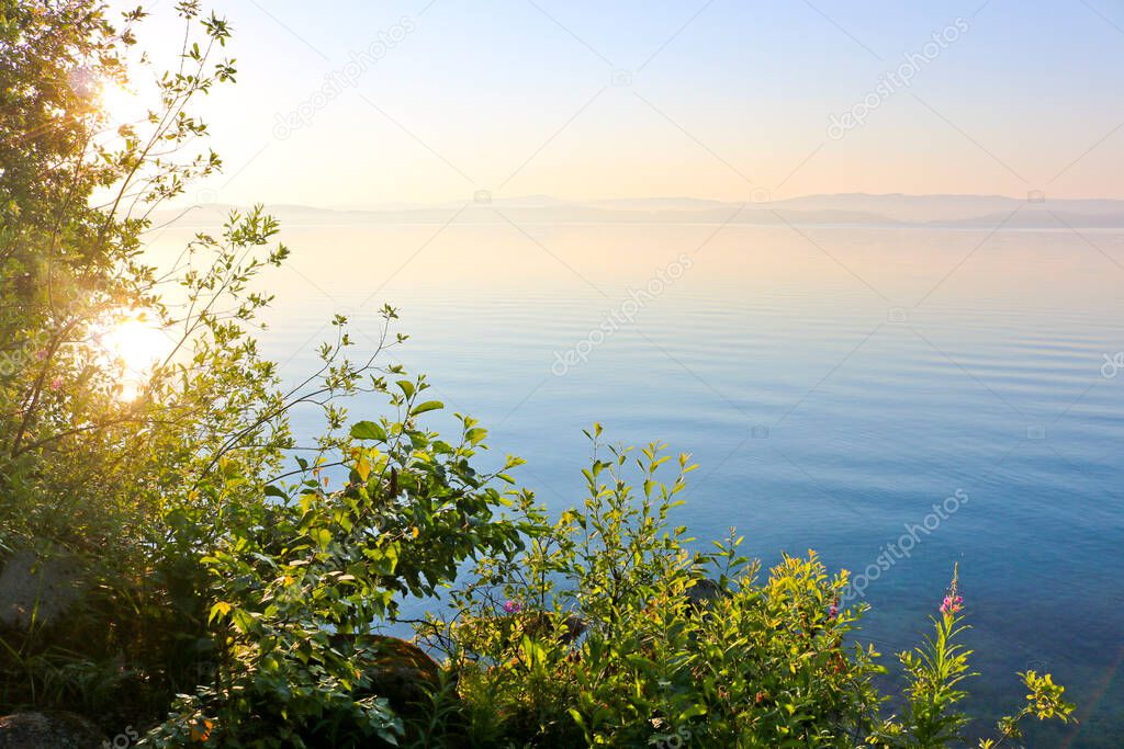 Dawn over the water surface of the lake. Calm, clear water. Turgoyak, Russia.