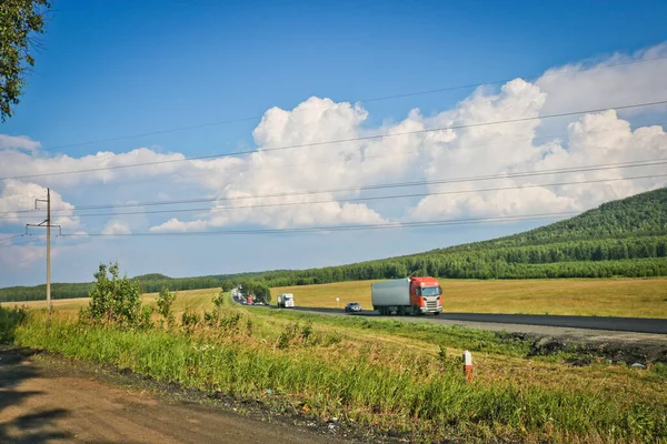 Highway with cars and trucks among fields and forests. Car travel concept.