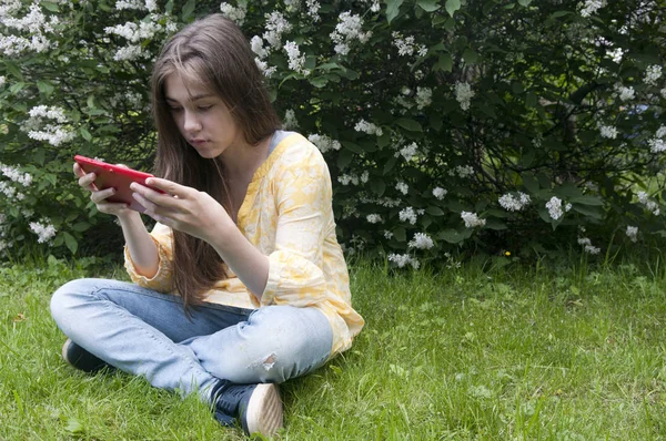 Hermosa chica adolescente con la tableta se sienta en el césped en el Parque. Foto: —  Fotos de Stock