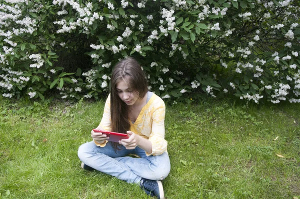 Hermosa chica adolescente con la tableta se sienta en el césped en el Parque. Foto: — Foto de Stock