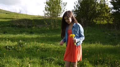 Kız sarı dandelions çayır on toplama. Dandelions. Bahar günü. Çiçekli bahar parkta güzel gülümseyen genç. Video çekim hareket kamera steadicam ile.