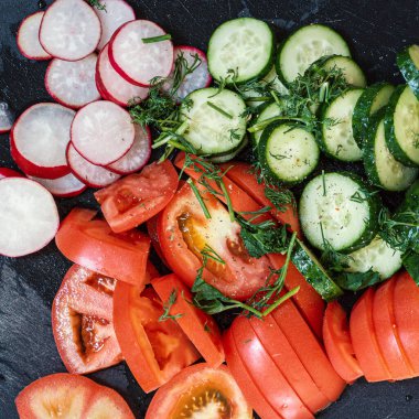 Dilimlenmiş domates, salatalık, turp ve otlarla dolu bir arka plan.