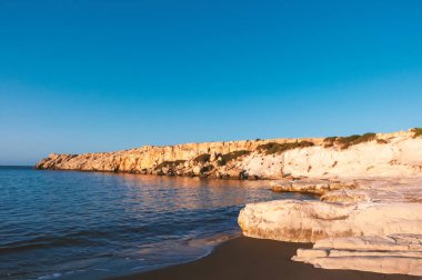 Terk edilmiş kayalık deniz kıyısı şafak güneşiyle aydınlanıyor.