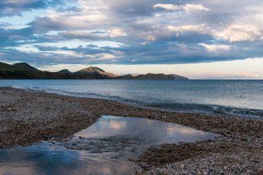 Gün batımında dağların arka planında terk edilmiş çakıl taşı plajı.