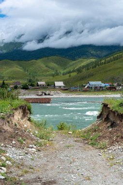 Altai Sibirya 'da bir köy ve ormanın arka planında dalgalı bir dağ nehri var.