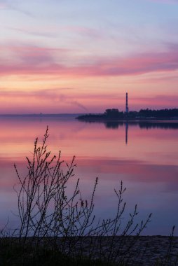 Baharda gölde gün batımı ön planda patlamamış çalılar ve arka planda kazan bacası ile