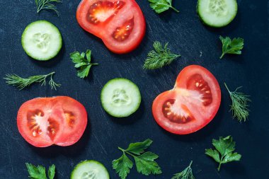 Siyah arka planda dilimlenmiş domates, salatalık, maydanoz ve dereotu.