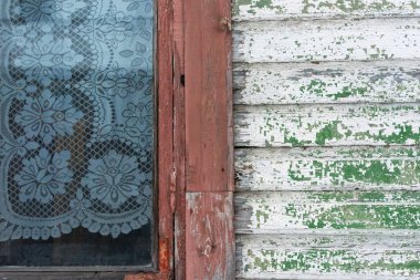 Eski ahşap bir duvarda dantel perdeli bir pencerenin ayrıntıları