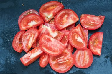 Dilimlenmiş domatesler koyu ıslak arka planda tuz serpiştirilmiş.