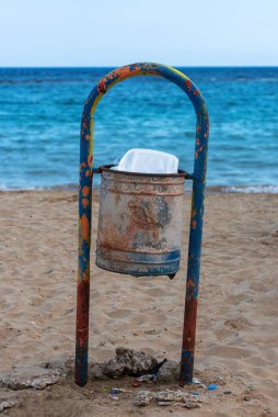 Kirli kumsalda paslı bir çöp tenekesi