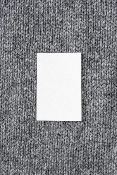 Winter holidays stationery mock-up scene. Blank paper greeting card, invitation against a background of gray knitted wool . Top view, copy space.