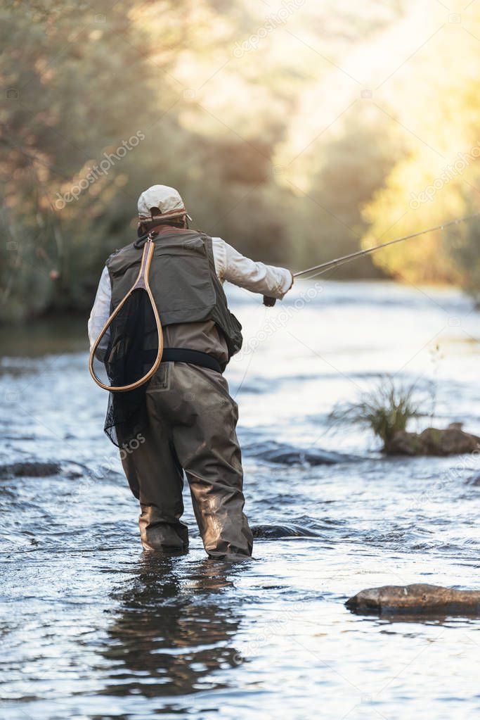 Fly fisherman using flyfishing rod in beautiful river