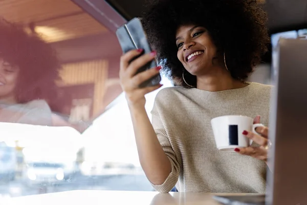 Portrait of attractive afro woman using mobile phone at the coffee shop. Business woman concept