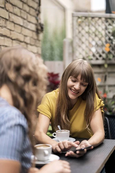 スマート フォンの共有と笑顔ながらカフェのテーブルでコーヒーを楽しむ現代の女性の友人 — ストック写真