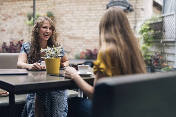 Stylish young women having friendly meeting with cups of coffee while sitting at table and chatting