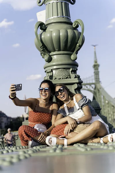 Χαρούμενες γυναίκες κάθονται στη γέφυρα και χρησιμοποιούν το κινητό — Φωτογραφία Αρχείου