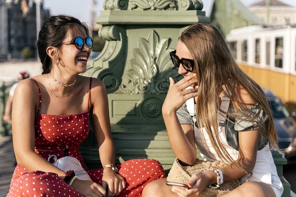 Cheerful women sitting on bridge and using cellphone — Stock Photo, Image