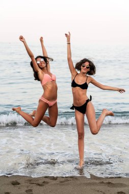 Okyanus sahilinde zıplayan gülen kadınlar