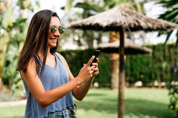 Mujer tomando fotos en un smartphone en un parque tropical — Foto de Stock