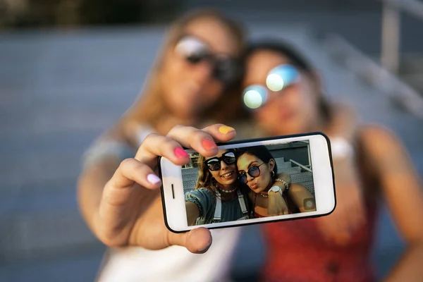 Wesołe kobiety siedzące na mostku i za pomocą telefonu komórkowego — Zdjęcie stockowe