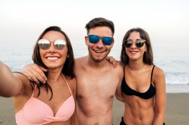 Okyanus sahilinde birlikte selfie çekerken sarılan genç arkadaşlar
